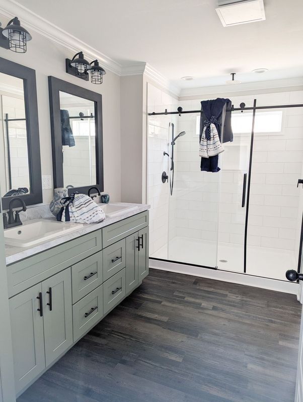 Modern bathroom with sage green double vanity, dark framed mirrors, and a glass-enclosed shower with white subway tile.