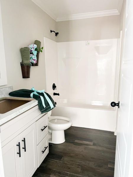 Modern bathroom with white vanity, dark flooring, and a white tub-shower unit, accented with green towels in wall planters.