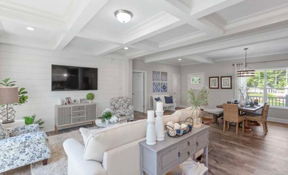 A bright, open-concept living and dining room with white shiplap walls, coffered ceilings, and light wood flooring.