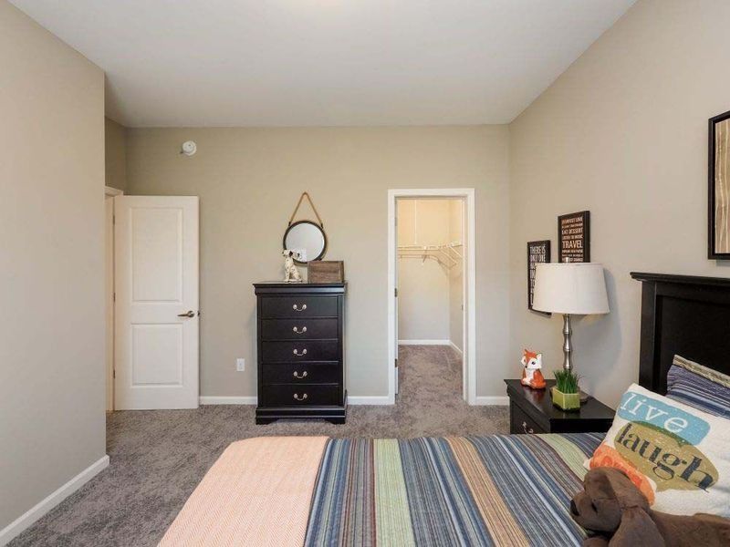 A bedroom with a dark wood dresser, a striped bedspread, a nightstand with a lamp, and an open closet door.