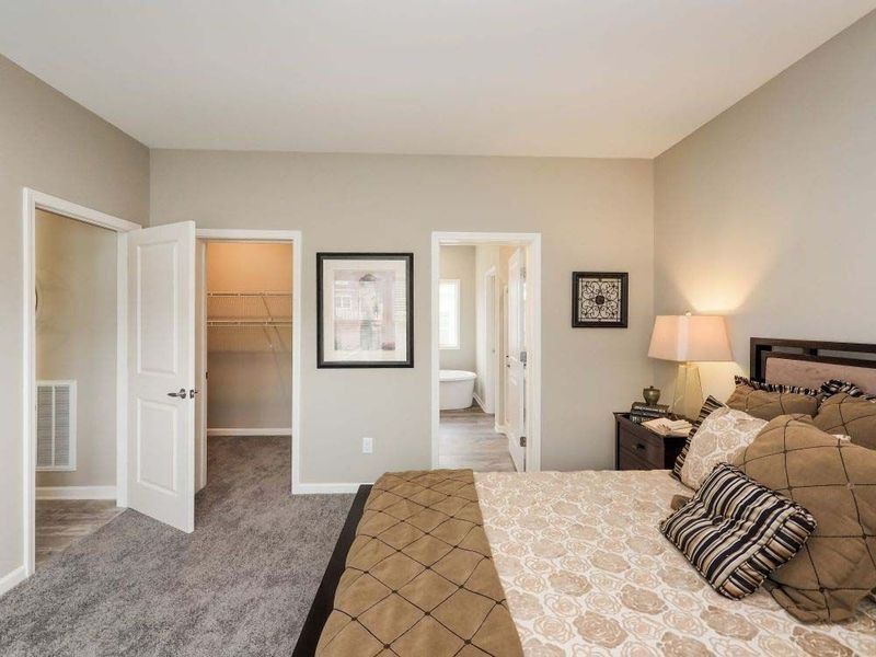 A bedroom featuring a bed with a brown quilt, two doorways leading to a closet and bathroom, and neutral-colored walls.