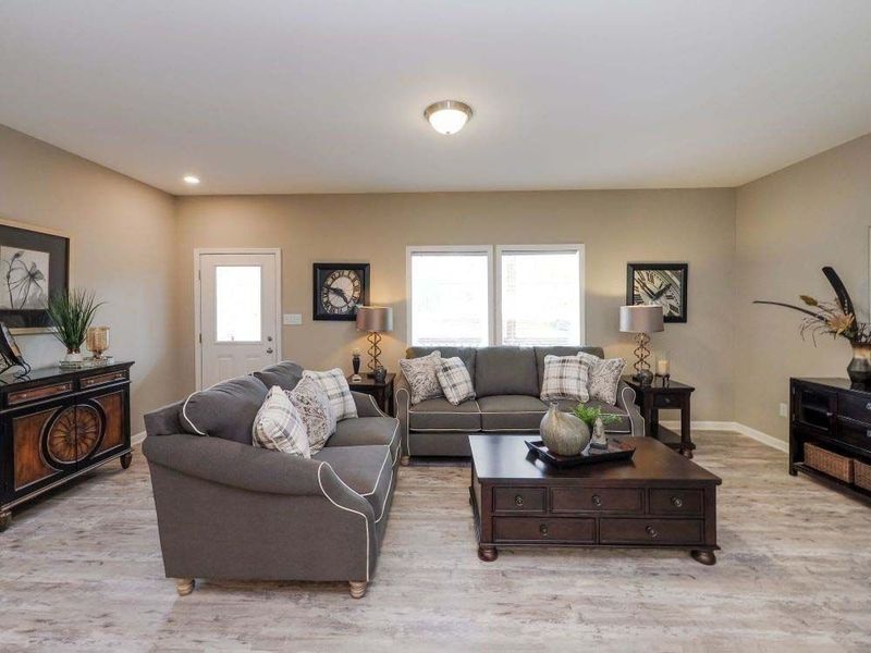 A living room with gray sofas, a dark coffee table, and wood-look flooring, illuminated by overhead ceiling lights.