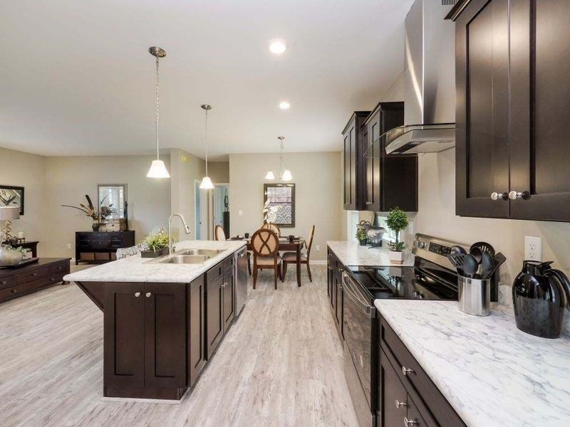 Modern kitchen with dark cabinets, a marble island, and light wood flooring, opening into a dining area and living room.