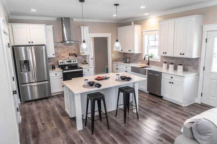 Modern white kitchen with a center island, stainless steel appliances, dark wood flooring, and pendant lighting.