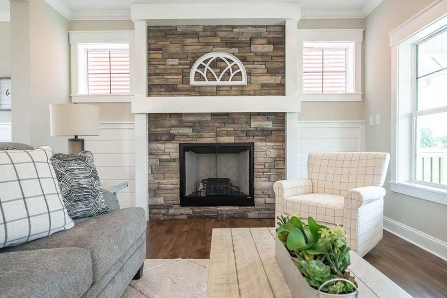 A living room featuring a stone fireplace with a white mantel, a grey couch, and a cream armchair.