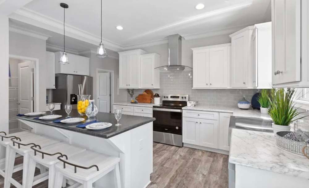 A modern kitchen with white cabinets, a dark island with three stools, stainless steel appliances, and wood-look flooring.