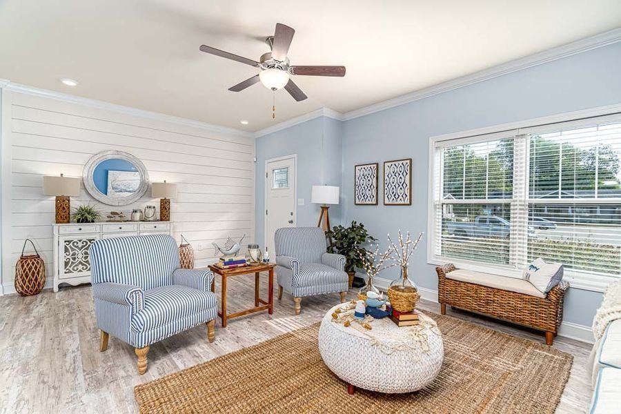 A bright sitting room with blue shiplap walls, two blue-striped armchairs, a woven rug, a white ottoman, and a wooden bench.