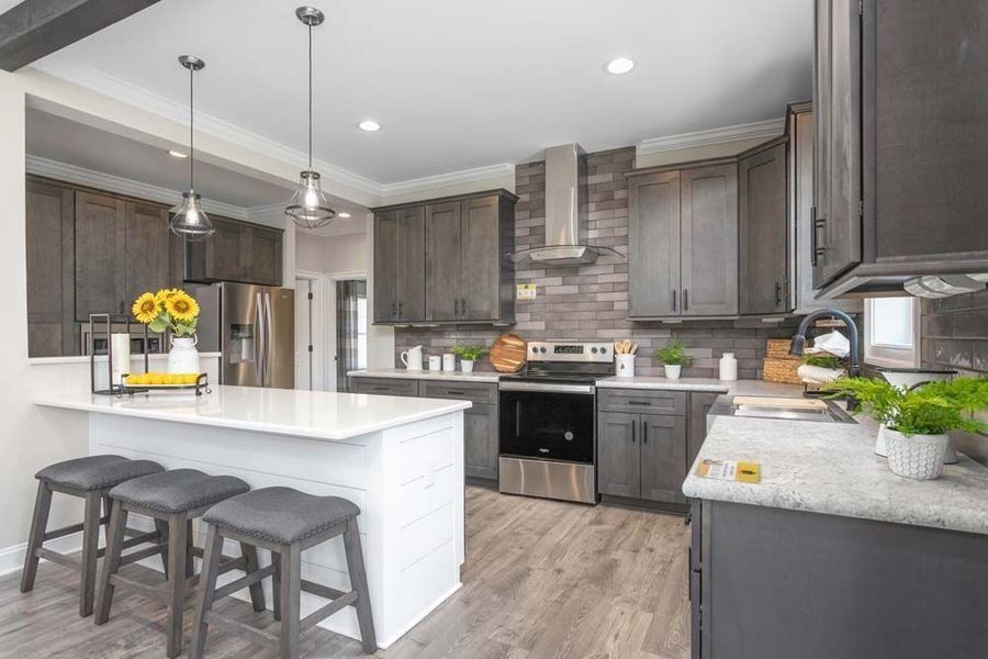Modern kitchen featuring dark wood cabinets, a white island with bar stools, stainless steel appliances, and wood floors.