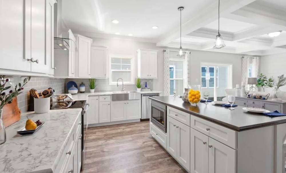 Modern white kitchen with a large island, marble countertops, stainless steel appliances, and wood-style flooring.