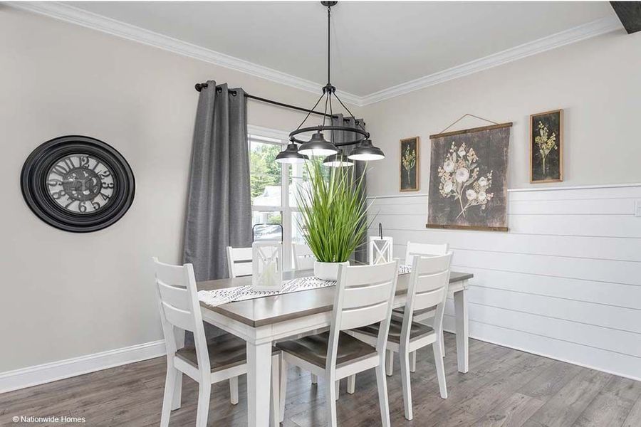 A dining area with a wood table, four white chairs, a pendant light, grey curtains, and white shiplap walls.