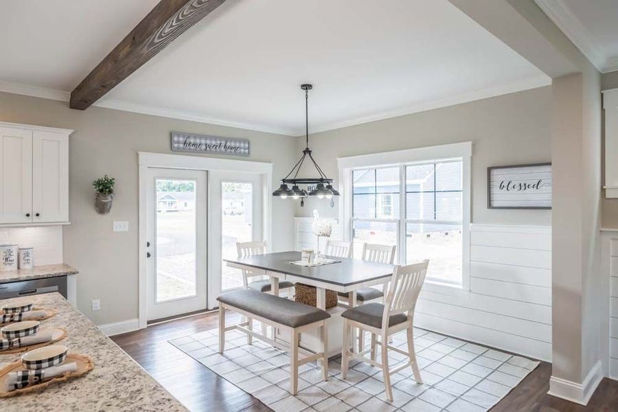A bright, neutral-toned dining area featuring a table, bench, two chairs, a chandelier, and wall-mounted decor.