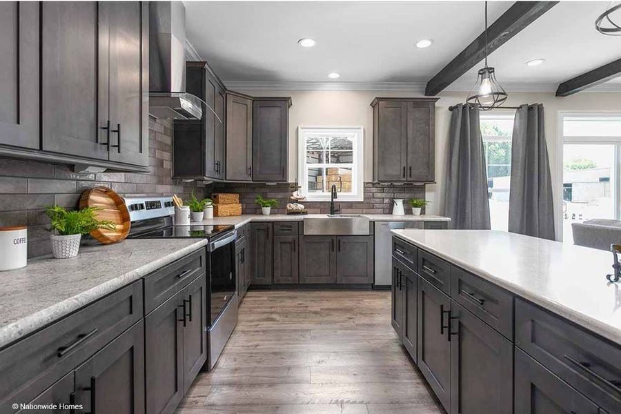A modern kitchen with dark gray cabinets, a white quartz island, wood-look flooring, and a farm-style sink.