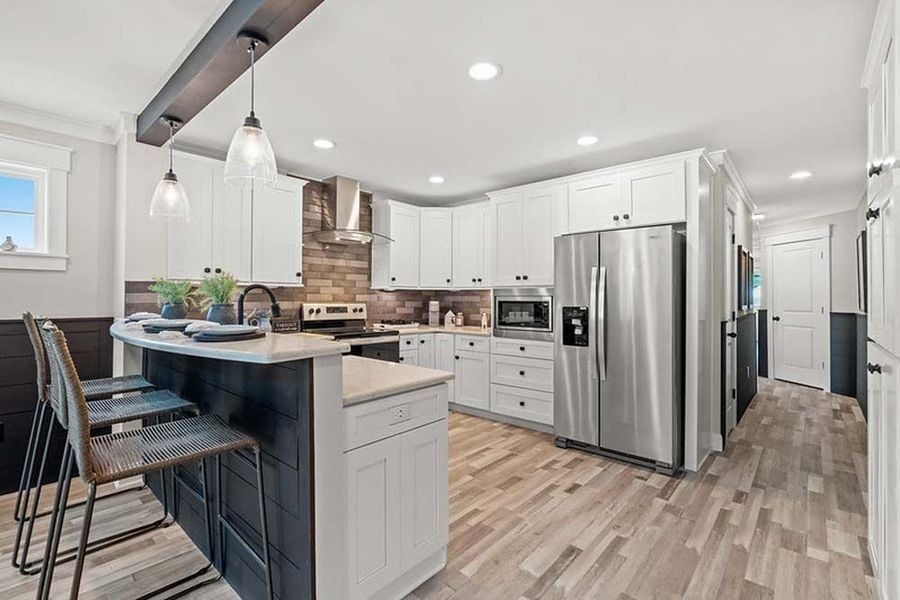 A modern kitchen featuring white cabinets, stainless steel appliances, wood-look flooring, and a dark island with bar stools.