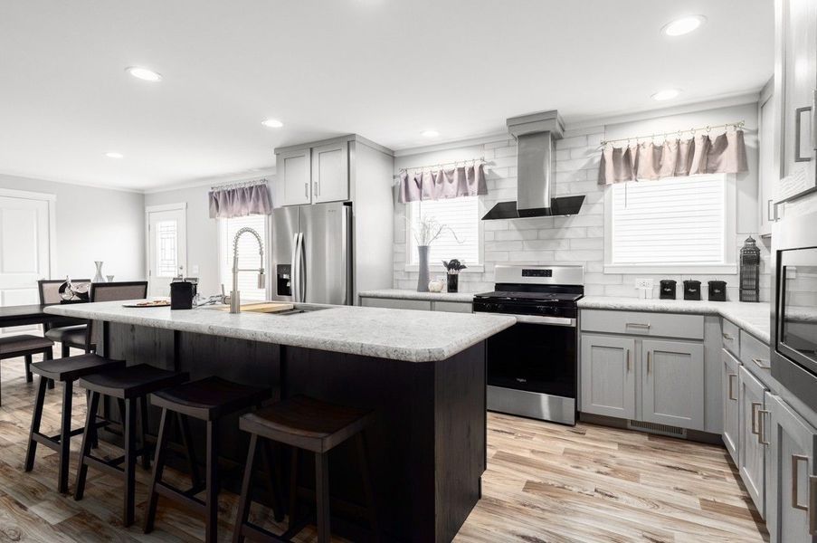 A modern kitchen featuring a dark island with bar stools, stainless steel appliances, and gray cabinetry.