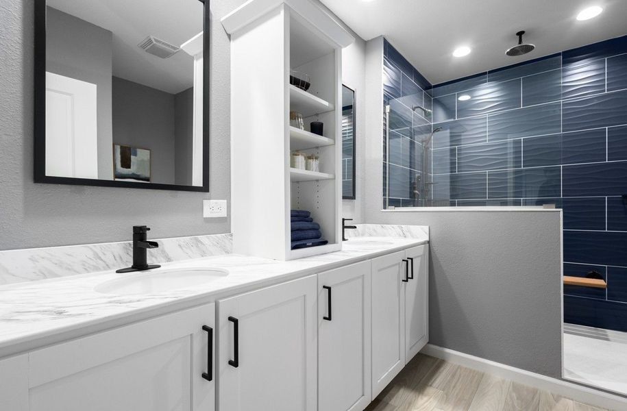 Modern bathroom with white cabinets, marble countertop, black faucets, and a shower with blue textured tile walls.