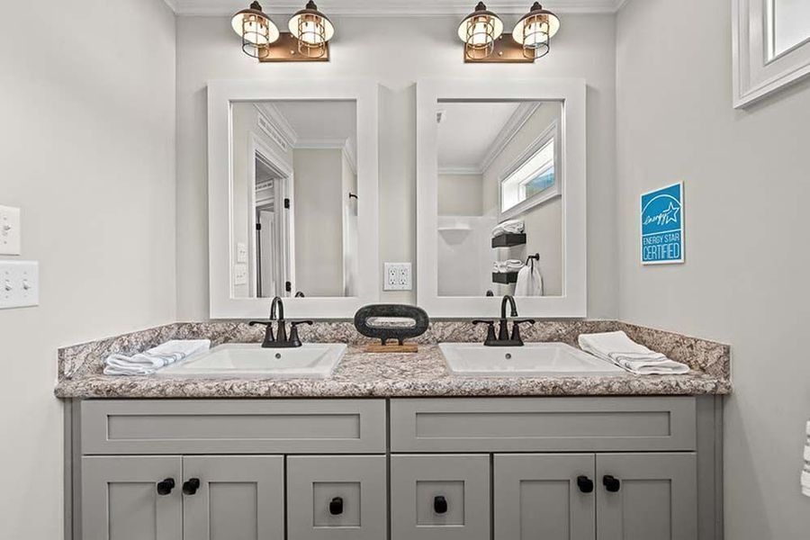 A modern bathroom vanity with gray cabinets, a speckled granite countertop, two sinks, and matching mirrors and lights.