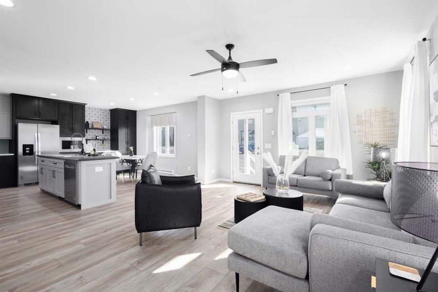 A modern open-concept home featuring a gray sectional sofa, black armchair, and a kitchen with dark cabinets and an island.