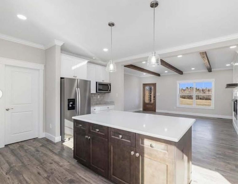 Modern kitchen interior with a central island, dark wood cabinets, white countertops, stainless steel fridge, and beams.