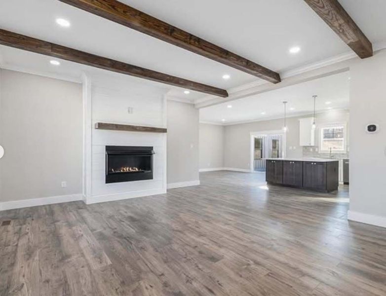 Open-concept living room and kitchen featuring wood-look flooring, exposed ceiling beams, and a modern fireplace.