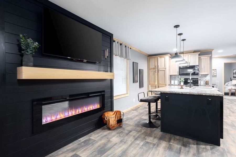 A modern living space with a black shiplap wall featuring a fireplace and mounted TV, next to a kitchen with an island.