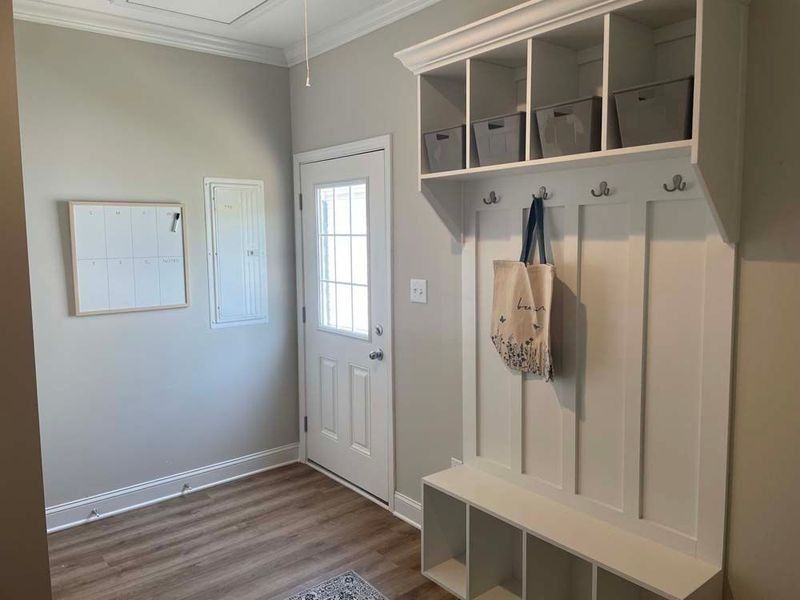 An entryway with light grey walls, wood-look floors, a white door, and a built-in white storage bench with cubbies.