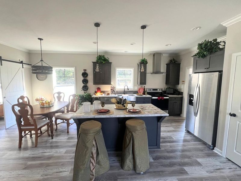 A modern kitchen featuring a marble-topped island with two draped stools, dark cabinets, stainless appliances, and dining.
