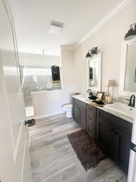 A modern bathroom with a dark wood vanity, white countertop, double sinks, a gray shower stall, and light wood flooring.