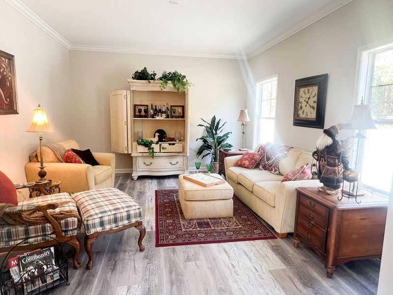 A living room with a beige sofa, patterned armchair with ottoman, wooden cabinet, and area rug on light wood flooring.