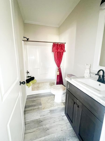 A modern bathroom with grey wood-look flooring, a vanity with a dark cabinet, and a shower with a red curtain.