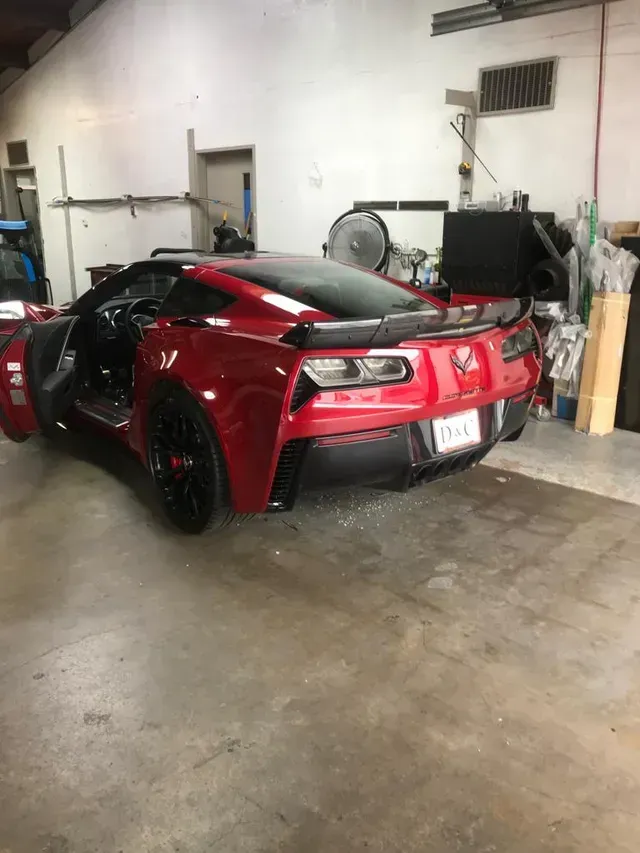 A red Chevrolet Corvette with its driver-side door open, parked inside a garage or workshop.