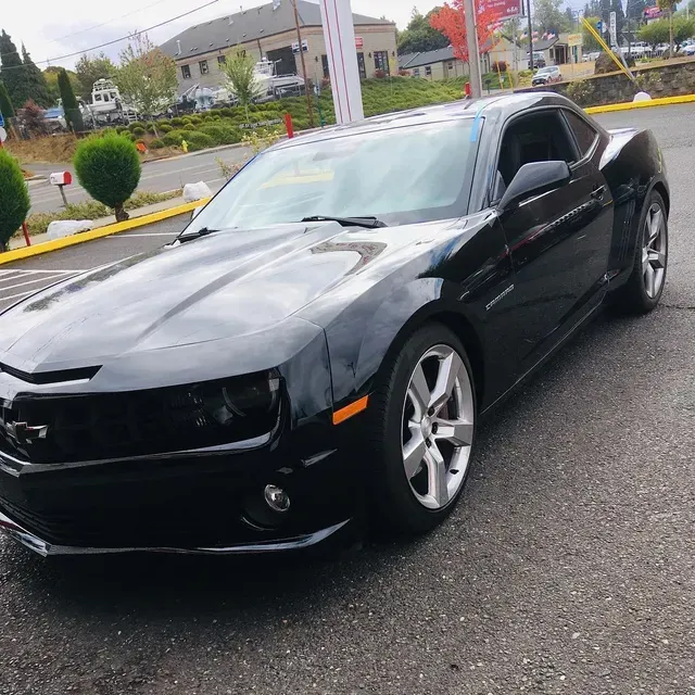 A black Chevrolet Camaro parked on an asphalt lot in front of a commercial building on a cloudy day.