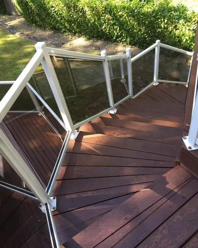 A high-angle view of brown wooden deck stairs with white railings and clear glass panels leading down to a garden.