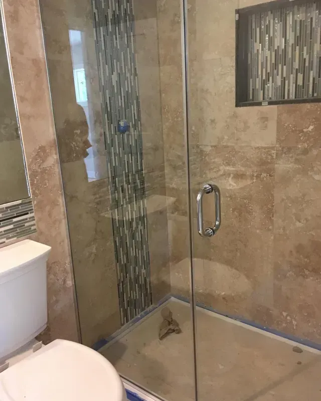 A bathroom with a beige tiled shower enclosure featuring a vertical blue mosaic tile accent and a glass door.
