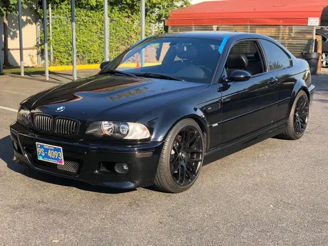 A black BMW M3 coupe parked outdoors on a paved lot on a sunny day.