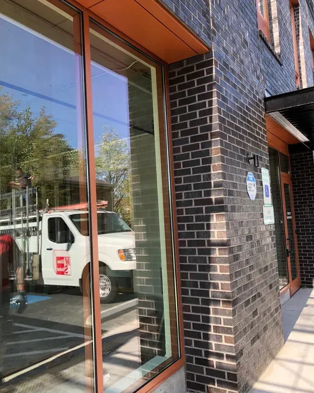 A brick building with large glass windows reflecting a white utility van parked in a lot outside.