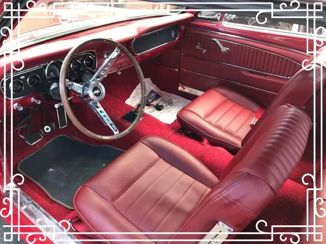 The interior of a classic red Mustang, featuring a red steering wheel, dashboard, and bucket seats with red carpeting.