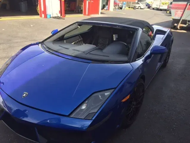 A blue Lamborghini convertible parked on an asphalt lot in daylight.