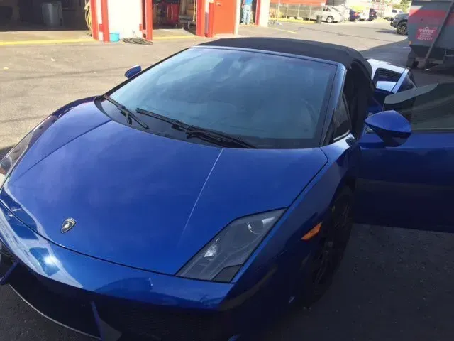 A bright blue Lamborghini convertible parked on an asphalt lot with its driver-side door open.