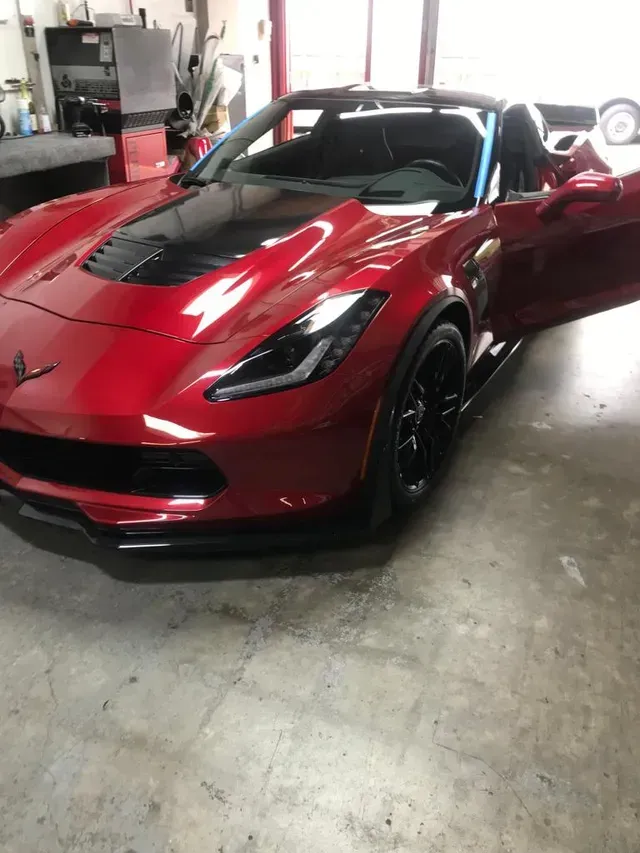 A red Chevrolet Corvette convertible with black accents parked inside a brightly lit garage.