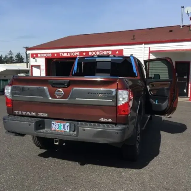 A brown Nissan Titan XD pickup truck parked outside a commercial building with its passenger door open.