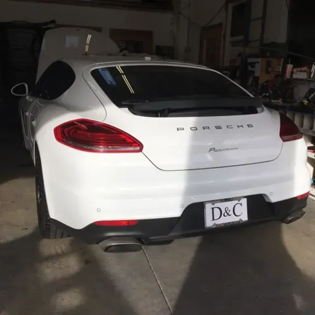 A white Porsche Panamera parked inside a garage, viewed from the rear with a license plate reading D&C.