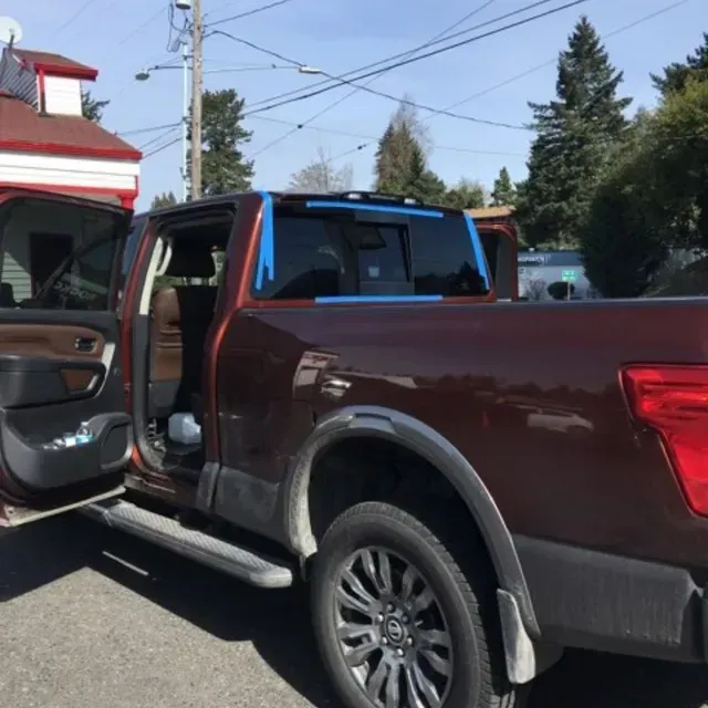 A brown pickup truck parked outdoors with blue painter's tape outlining the rear window.