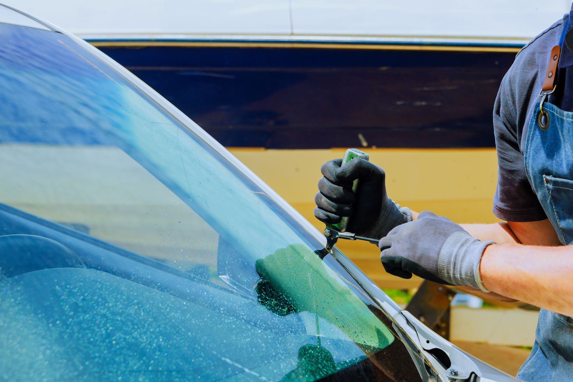 Person wearing gloves cleaning a car windshield with a green sponge.
