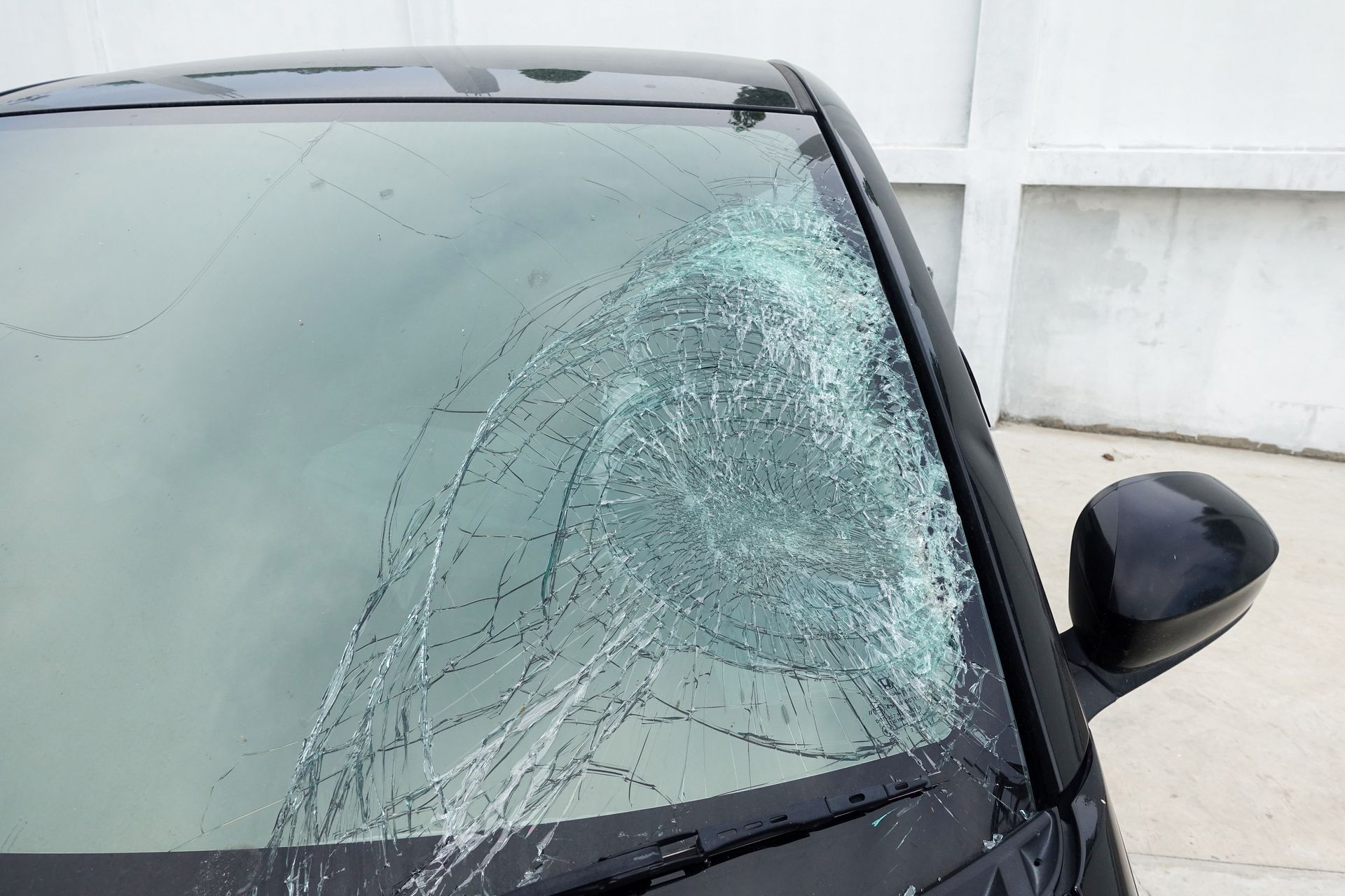 A black car with a large, spiderweb-pattern crack across the passenger side of the windshield.