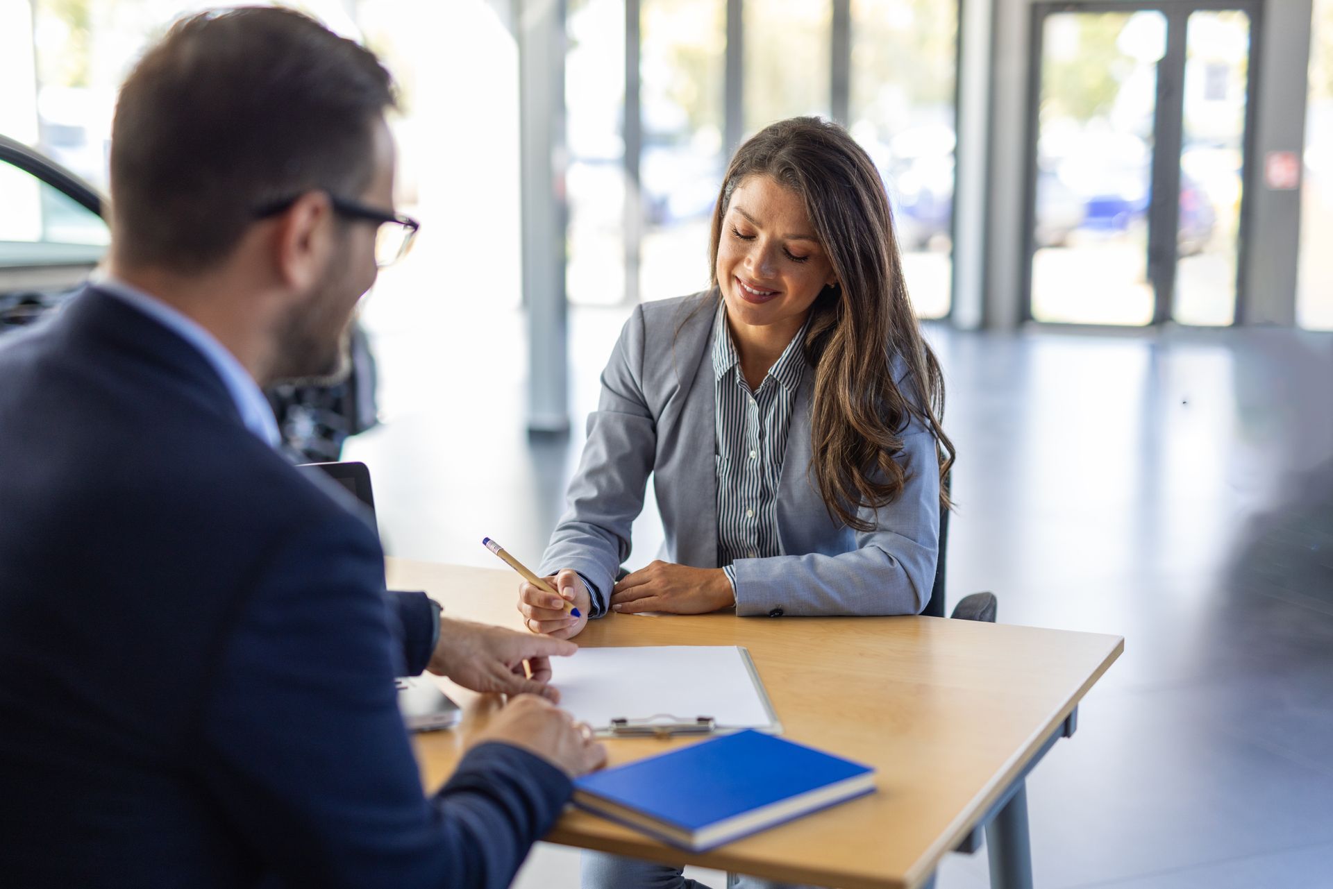 A professional man and woman sit at a desk, reviewing a document together in a bright, modern office space.