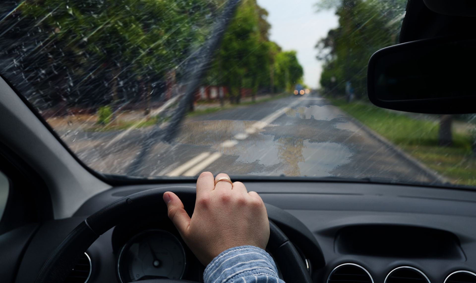 A view from inside a car driving on a rain-slicked road with windshield wipers active.