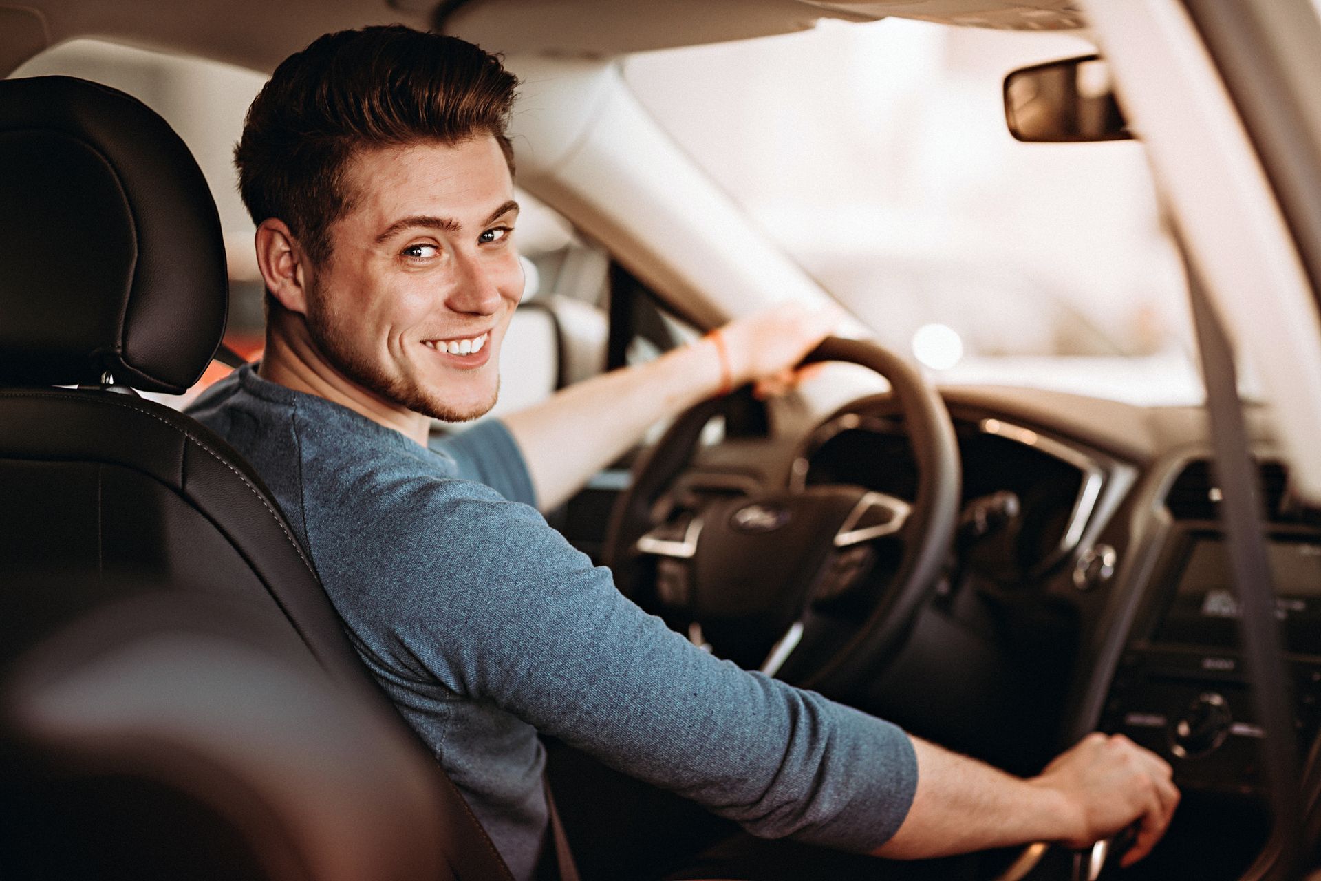 A person smiling while driving a car, looking back over their shoulder.