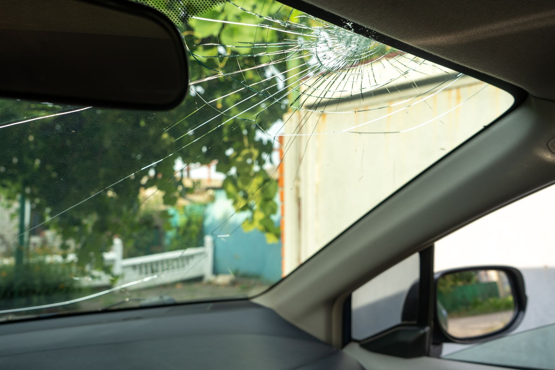 A view from inside a car showing a severely cracked windshield with a spiderweb-like impact point.