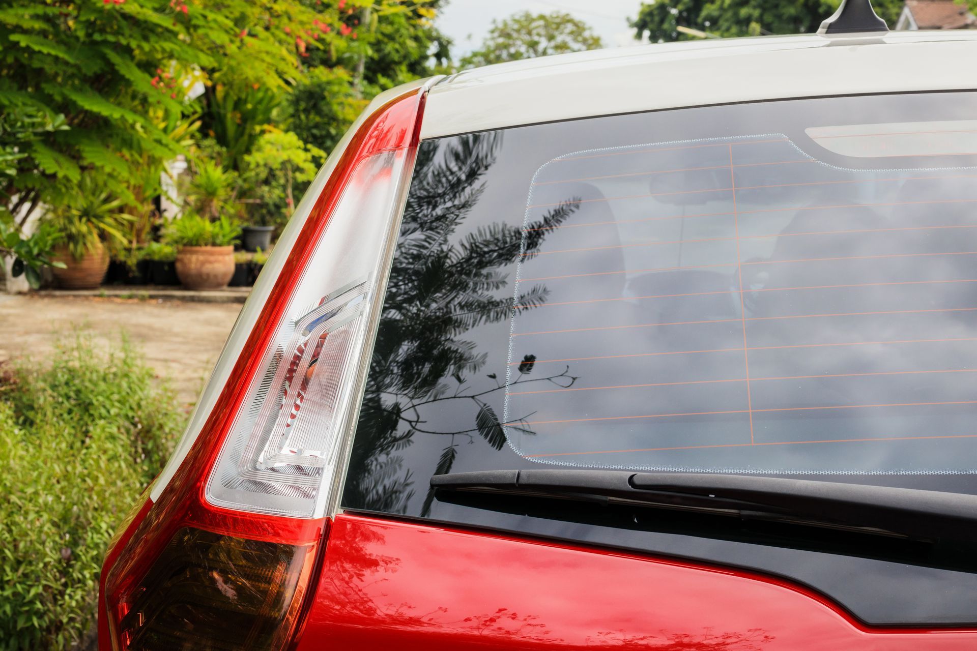 Red and white car's rear, with a window and a taillight, parked outdoors, green foliage in the background.