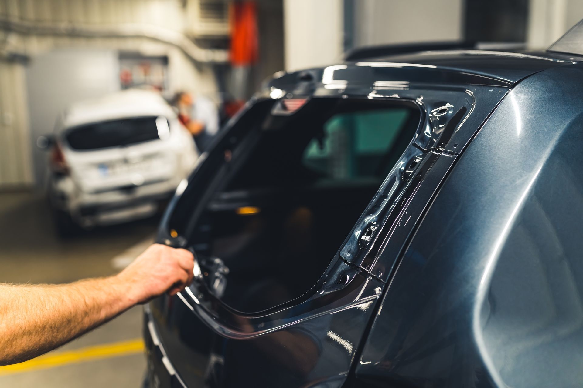 A technician applies adhesive to the frame of a car's rear window in a garage.
